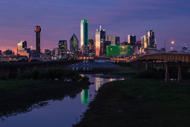 A view of a waterway surrounded by bridges on both sides in Dallas, Texas, showing the skyscrapers during the night